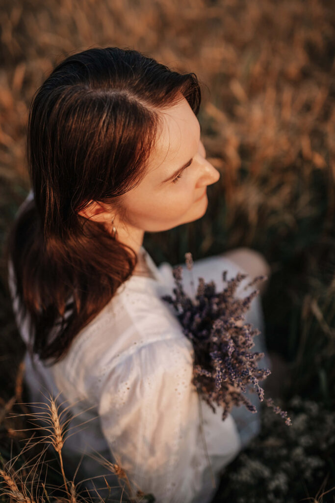Tania sitting in a field holding a bouquet of dried flowers during sunset.
