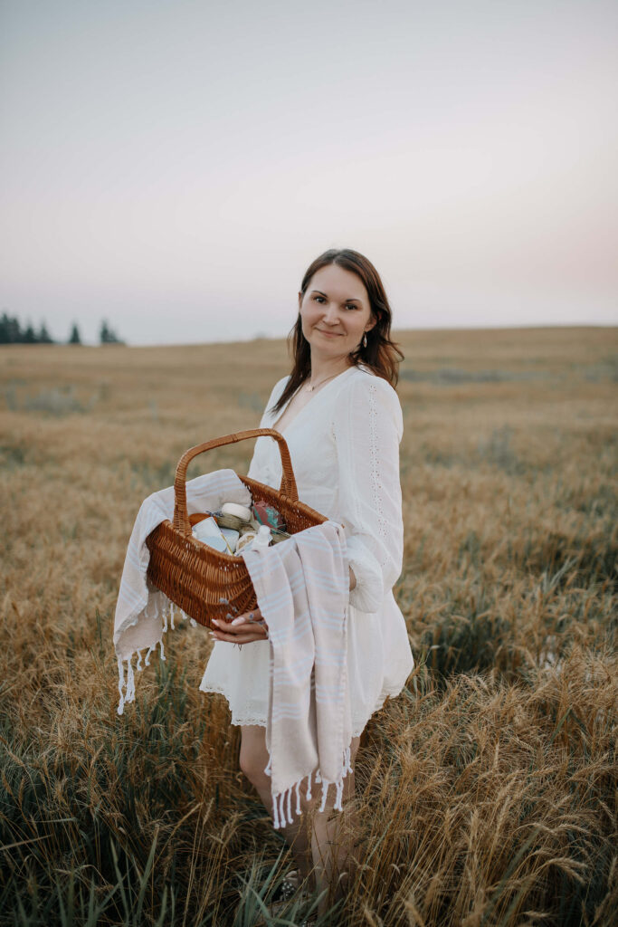 Tania in a white dress with a basket of her natural cosmetics, posing in a field during a beautiful sunset.