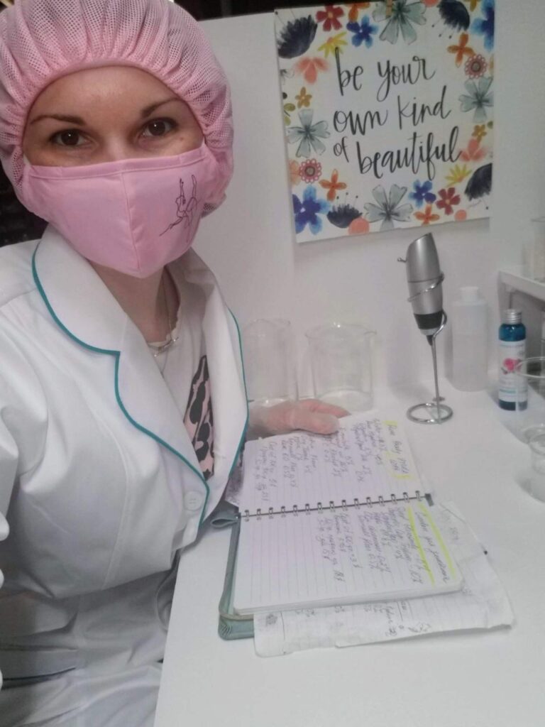 Tania in white lab coat, mask, and cap, meticulously overseeing production in her cosmetics lab.